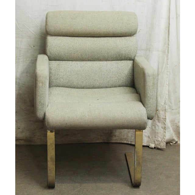 Gray upholstered chair with brass finished metal legs. There is wear and some staining. The manufacturer and exact date of...