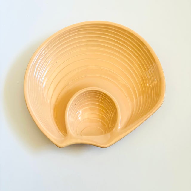 A vintage ceramic chip and dip tray in the shape of a seashell. Features a smaller inner bowl formed on one side. Ribbed...