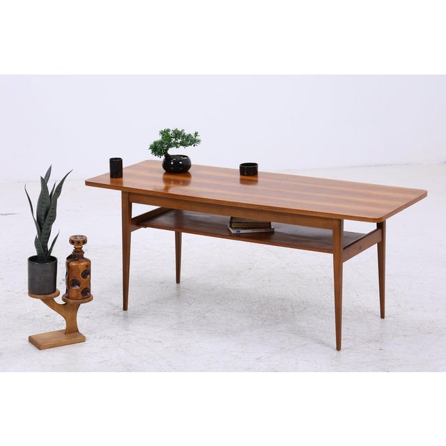 A beautiful coffee table in a classic mid-century style with slender, tapered legs and a practical shelf. The understated...