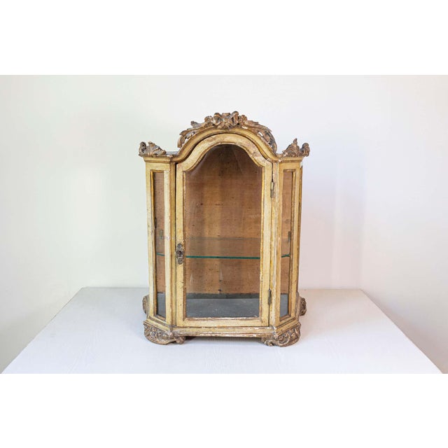 A petite Venetian 18th century period Rococo painted wood vitrine with carved crest and glass door. Created in Italy...