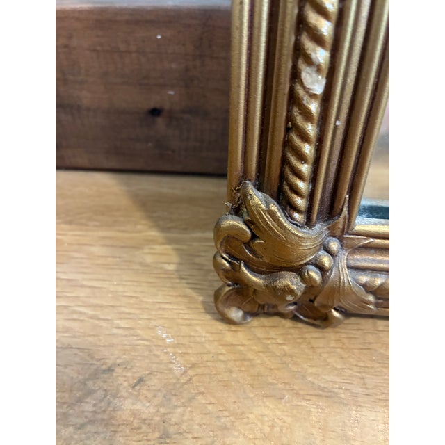 Stunning vintage gold wall mirror featuring an ornate carved frame with laurel wreath crest, scrolling corners, and...
