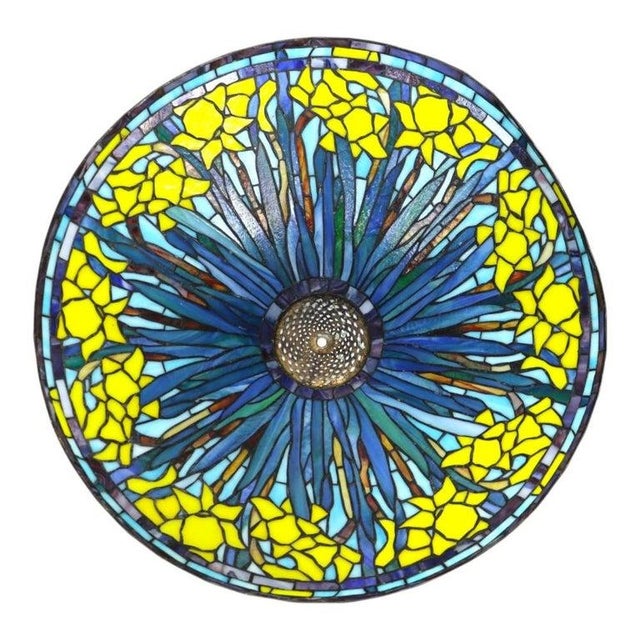 A striking Tiffany style leaded stained glass table lamp, featuring a conical shade adorned with a vibrant daffodil motif....