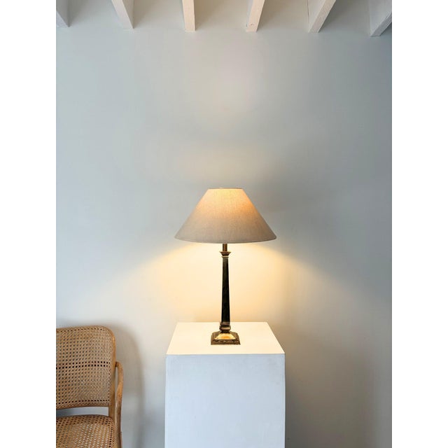 A solid brass vintage table lamp with a classical column form and a timeworn patinated finish. The squared stem sits on a...