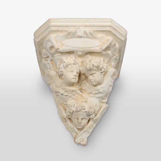 An antique French church wall console in plaster featuring three cherubs or angels with decorations. This rustic console...