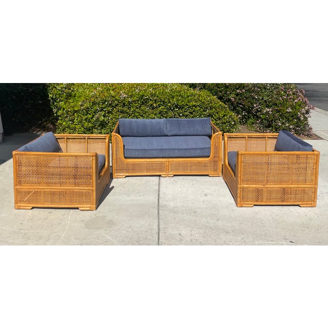 A 70s chic, vintage rattan lounge set featuring a loveseat and matching pair of club chairs. The low profile frames are...