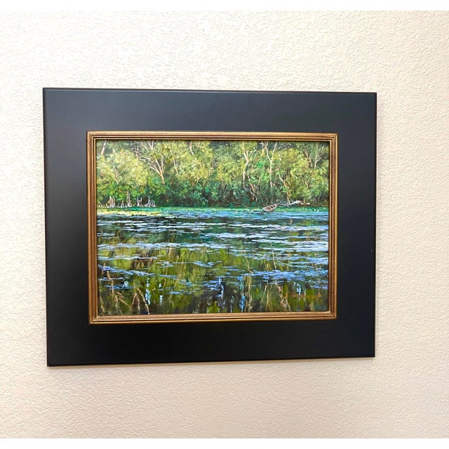 This oil painting captures a serene waterscape, where lush greenery frames a tranquil pond dotted with lily pads. The...