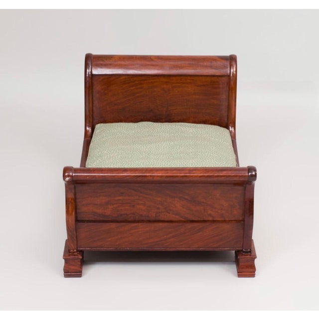 The diminutive mahogany sleigh bed with green and white upholstery. The piece is from the late 20th century.