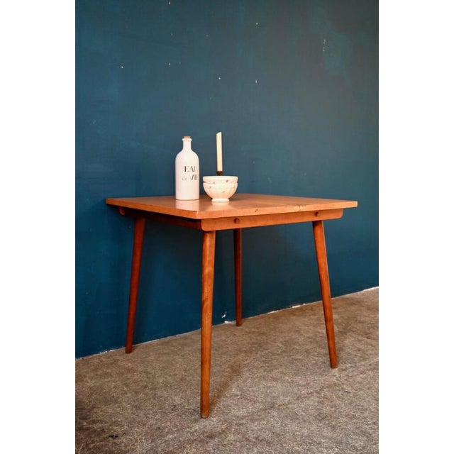 Square and small in size, this retro table from the 60s is entirely made of wood. Its spindle base is thin and elegant....