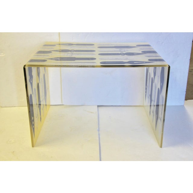 Handsome waterfall acrylic coffee table in the manner of Piero Fornasetti. Features a graphic transfer print of oversized...