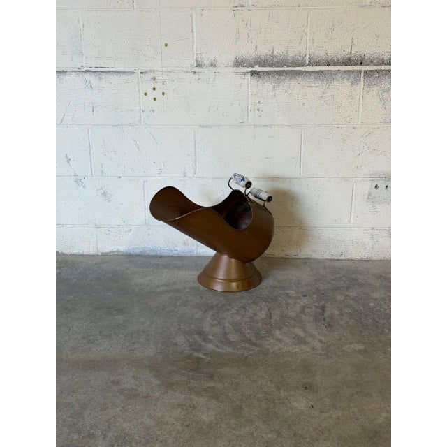 This hammered copper firewood holder features a sculptural pedestal base and contrasting blue-and-white patterned ceramic...