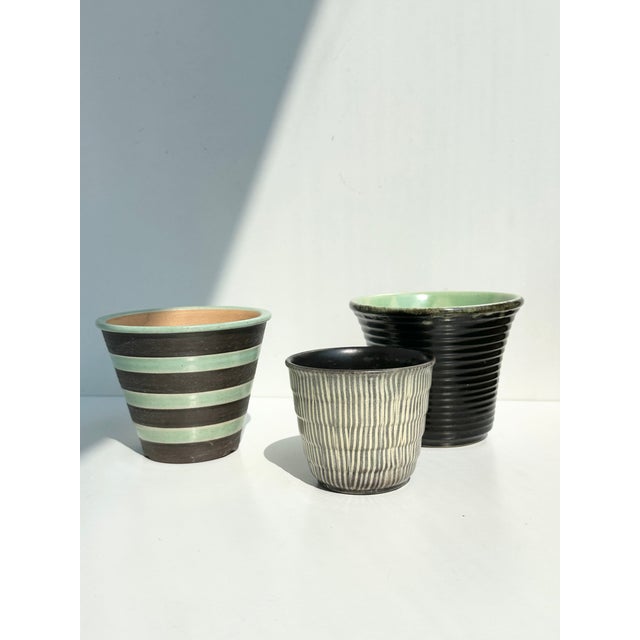 A rare and color-coordinated set of three plant pots from the 1950s: a horizontally striped, hand-thrown piece from veb...