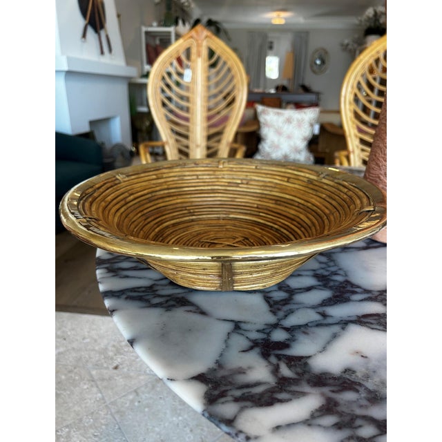 A vintage pencil reed rattan bowl with brass trim, defined by its coiled construction and warm natural tone. The form is...