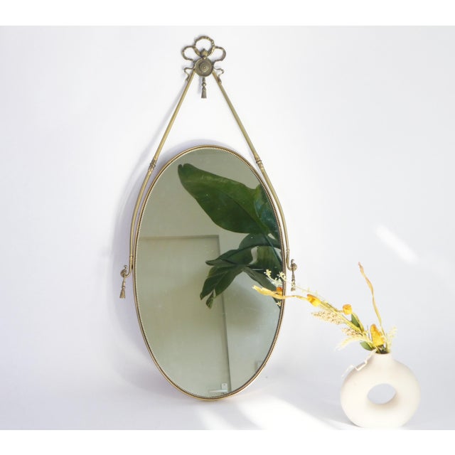 Stunning Italian oval brass wall mirror. The mirror has a nice brass cord with a wonderful ornament in the form of a...