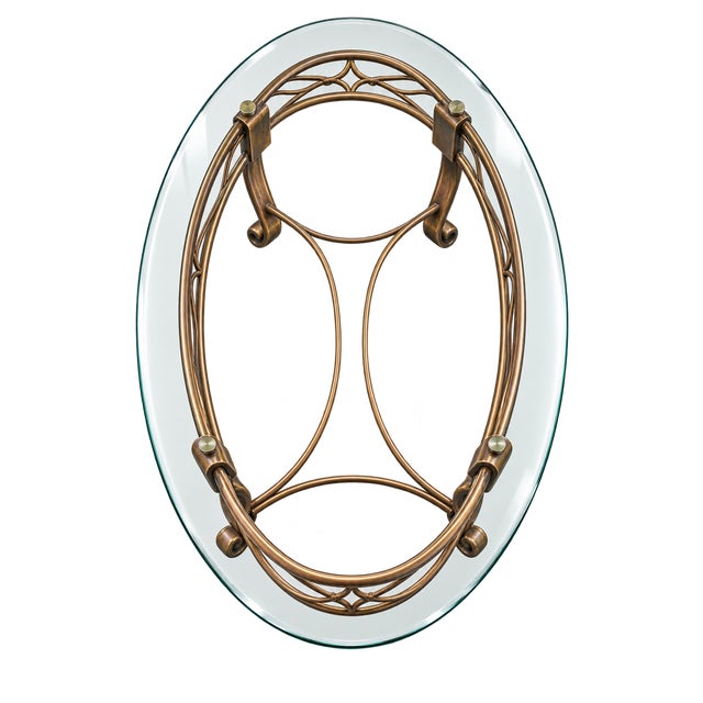 Elegant vintage Hollywood Regency–style coffee table featuring an oval glass top and an ornate gilt metal base. The base...