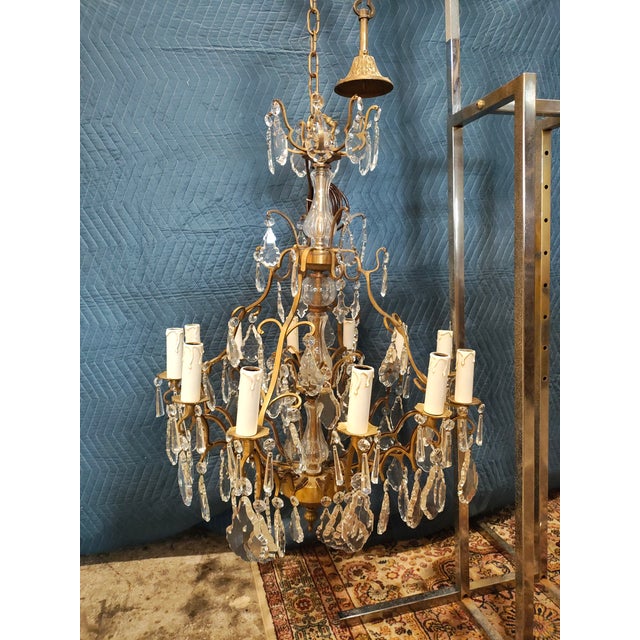 A striking vintage French Louis XV–style chandelier featuring twelve lights arranged across two graceful tiers. The warm...