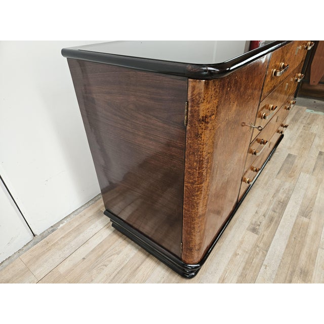 An elegant 1950s Italian Art Deco sideboard, featuring a refined burl veneer and elegant black lacquered wood details that...