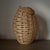 A sculptural oval lantern by Two’s Company, crafted in handwoven natural rattan and finished with a warm faux leather...