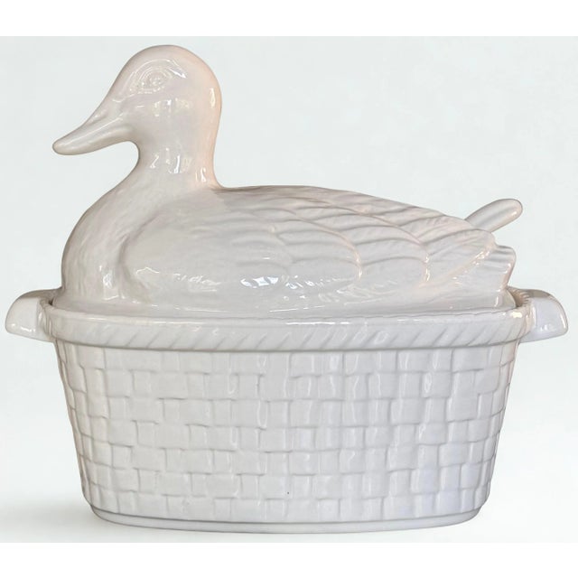 By Whittier Potteries, Califorina, U.S.A., an all-white painted and glazed duck sits upon a Trompe L'Oleil basket. Order...