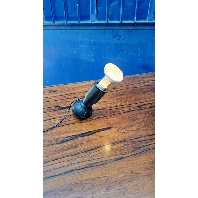Lamp designed by Gino Sarfatti for Arteluce in 1966. Black lacquered aluminum bulb holder. Black skai base filled with...
