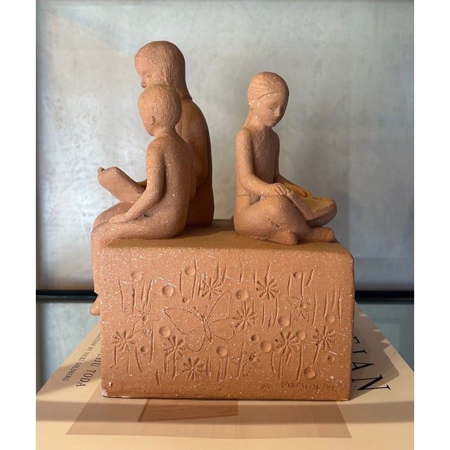 Terracotta sculpture by artist Marilyn Fox. Scene is of a mother and two children reading along with their cat. The base...