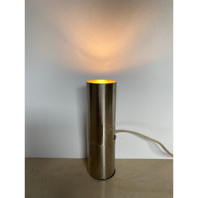 Vintage mid-century modern accent lamp in brushed metal, featuring a sleek, minimalist tubular cylinder housing on a small...