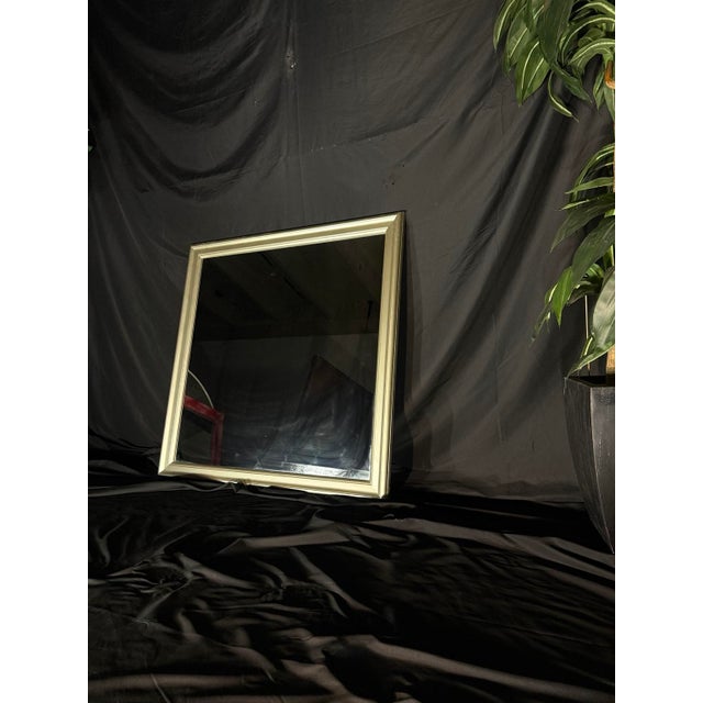 Square wall mirror with a substantial frame in a soft champagne-silver / light gold-tone metallic finish and a clean...