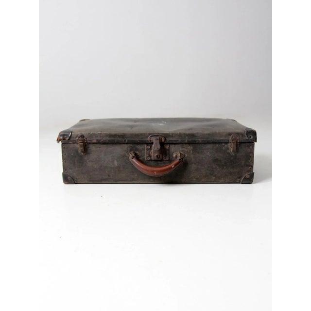 A vintage 1920s–1930s hardboard suitcase with a faded black exterior and classic travel-era construction. Features...