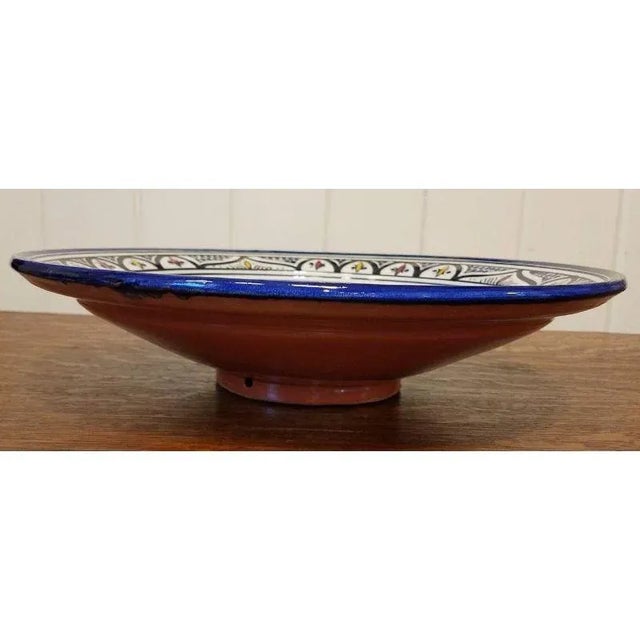 Large-scale terracotta bowl with bright blue, yellow, and red geometric patterns. An ornamental piece that is refined with...