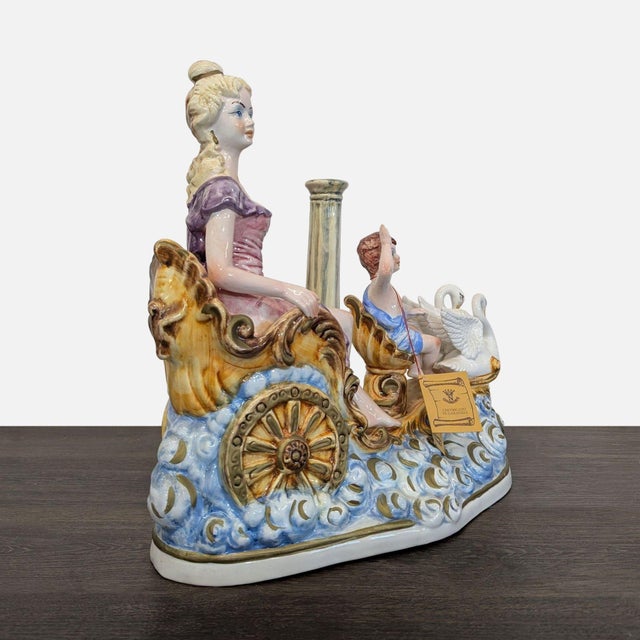 This Capodimonte sculpture features a graceful lady seated in a decorated chariot, accompanied by a cherub and a swan....