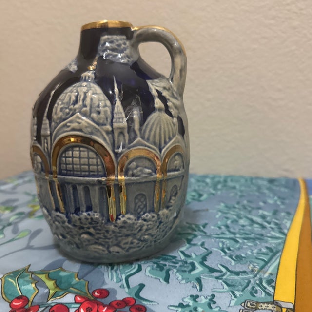 Features a cobalt blue glaze with gold and white embossed detailing of a European cathedral or city scene, often...