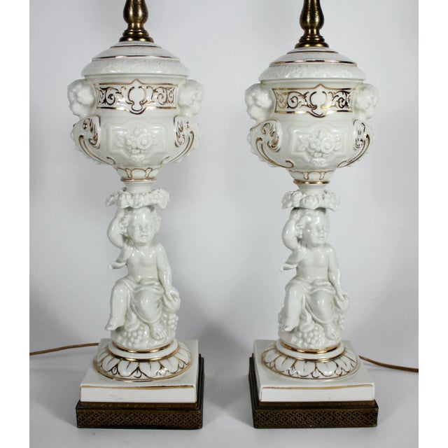 Pair of 20th century parcel-gilt porcelain table lamps taking the form of seated cherubs. Pierced brass bases. Unsigned....