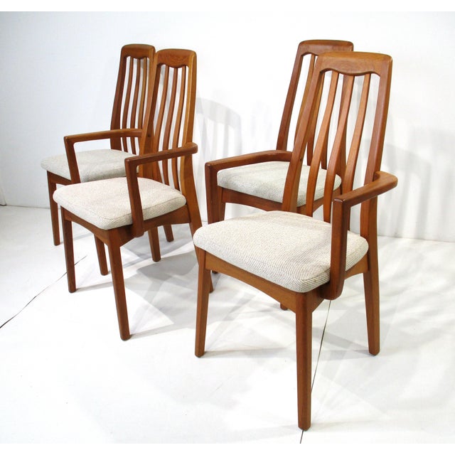A set of four teak wood framed dining chairs two with arms and two sides all with upholstered seats in a tight woven...