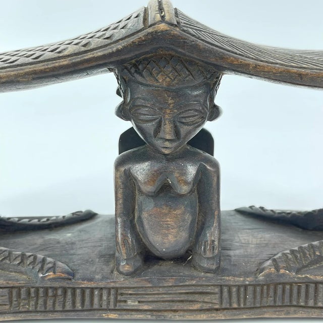 A carved double headrest from the Songye people is a sculptural sleeping support traditionally used in the savanna regions...