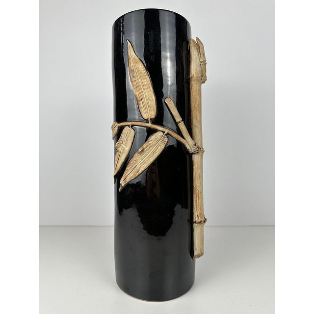 Stylish ceramic vase with a sleek, cylindrical design in glossy black. The vase is decoratively finished with a refined...