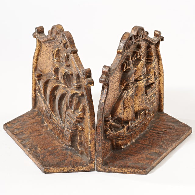 These vintage iron bookends have a gold paint overlay that shows wear and age. Stamped on the back side of the bookends...