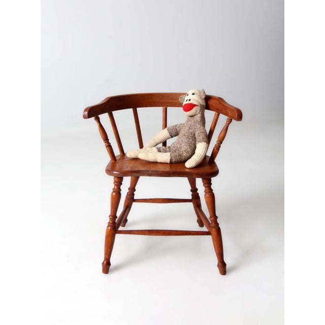A classic vintage Windsor child’s armchair featuring a gently curved crest rail and traditional turned spindle back....