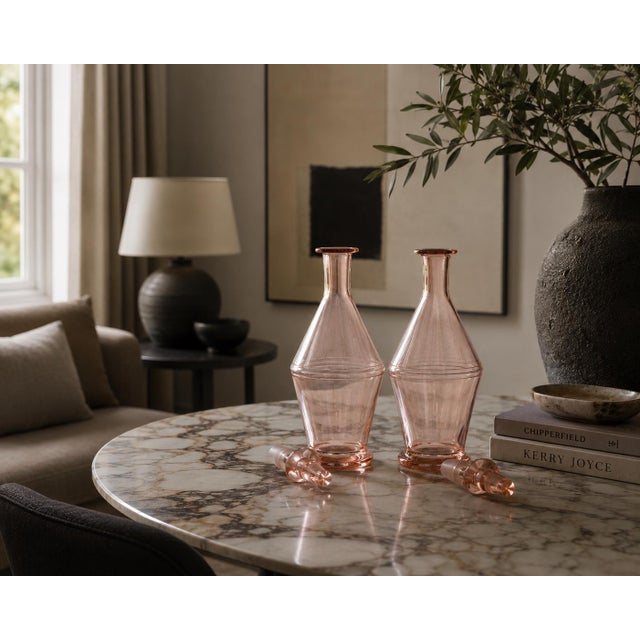 Pair of French pink glass carafes dating to the 1960s, with an Art Deco-inspired silhouette. Each has a shaped body...