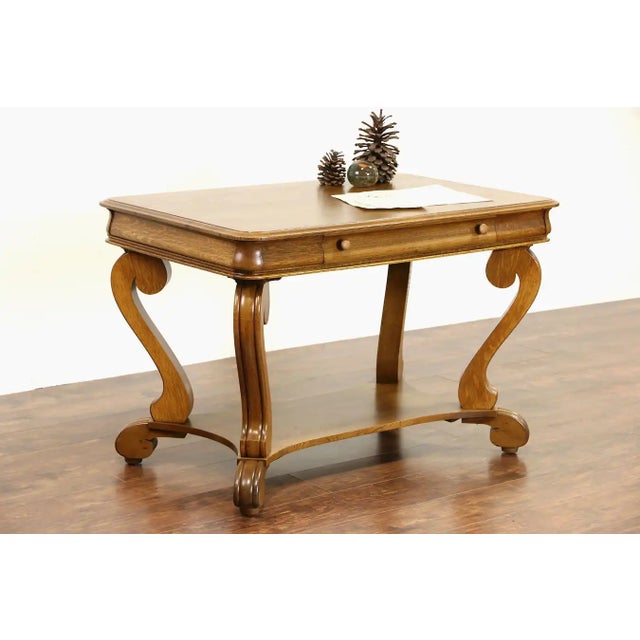 A library table or writing desk from the early 1900's was carved Mahogany in the Empire style with curving scrolled legs....