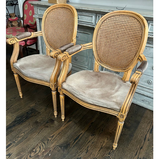 Elegant pair of Louis XVI–style armchairs featuring classic carved beech wood frames, double-caned backs, and nailhead...