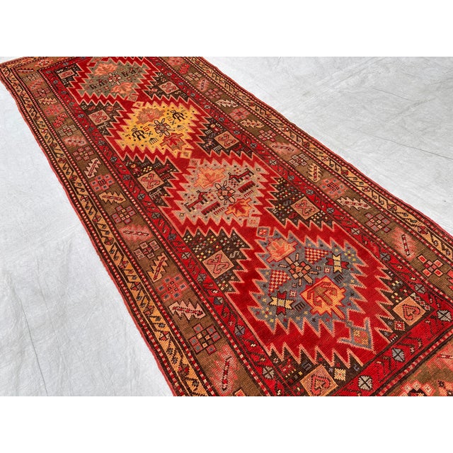 This antique hand-knotted Karabagh runner features four bold serrated diamond medallions in red, gold, and slate blue,...