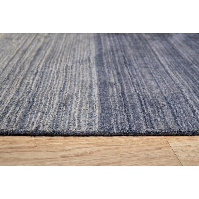 This blue wool rug features a hand knotted pile construction that blends traditional craftsmanship with contemporary...