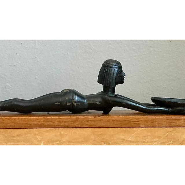 This vintage Egyptian-inspired metal figure is mounted on a rectangular wooden base and presents a stylized, elongated...