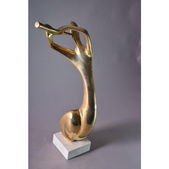 This sculpture reduces a musician to a single continuous gesture — one sweeping brass line running from an outstretched...