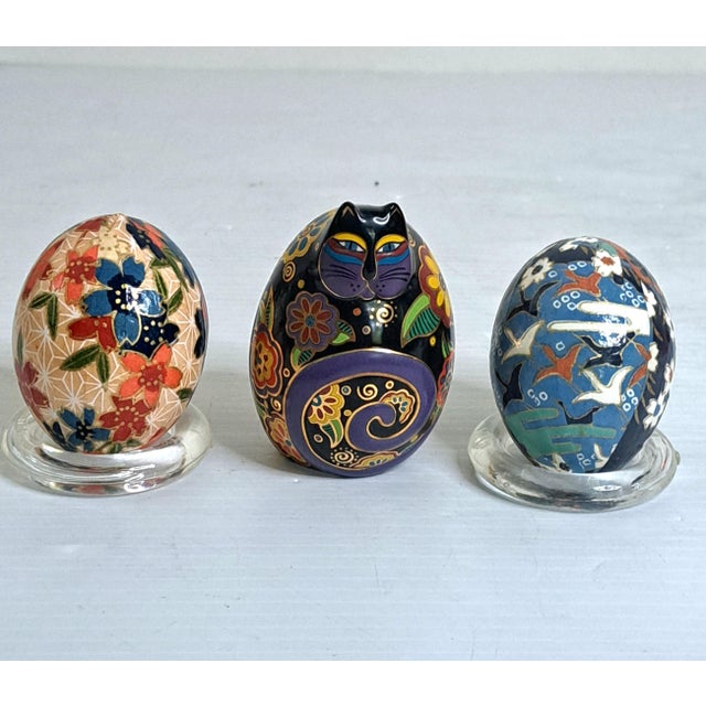 A cheerful vintage decorative trio pairing a signed 1996 Laurel Burch “Flowering Feline” ceramic cat with two Japanese...