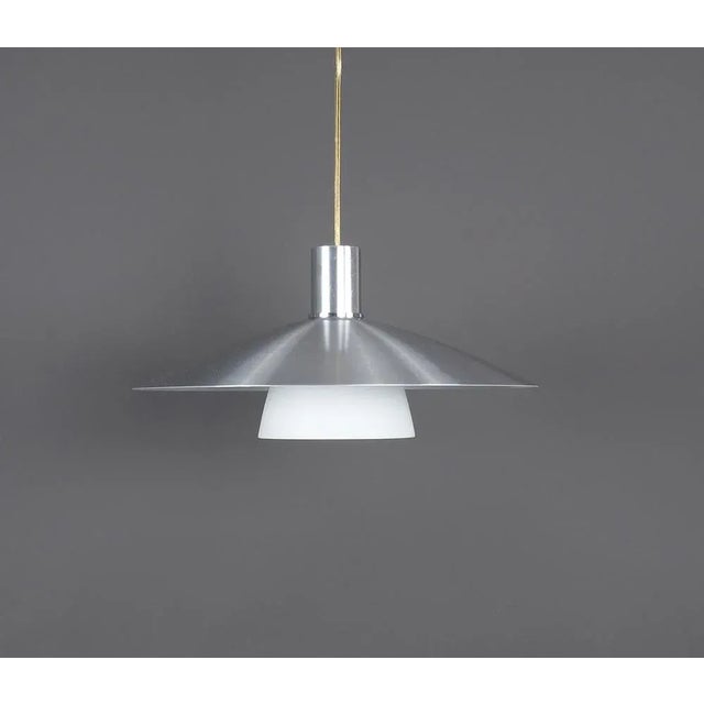 Metal hanging lamp with milk glass produced by Belid Denmark in the 1980s. The lamp has a silver bowl with a white milk...
