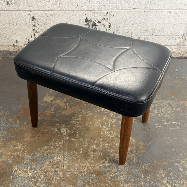 A vintage Danish modern stool from the 1960s with a black leather upholstered seat and tapered teak legs. The design is...