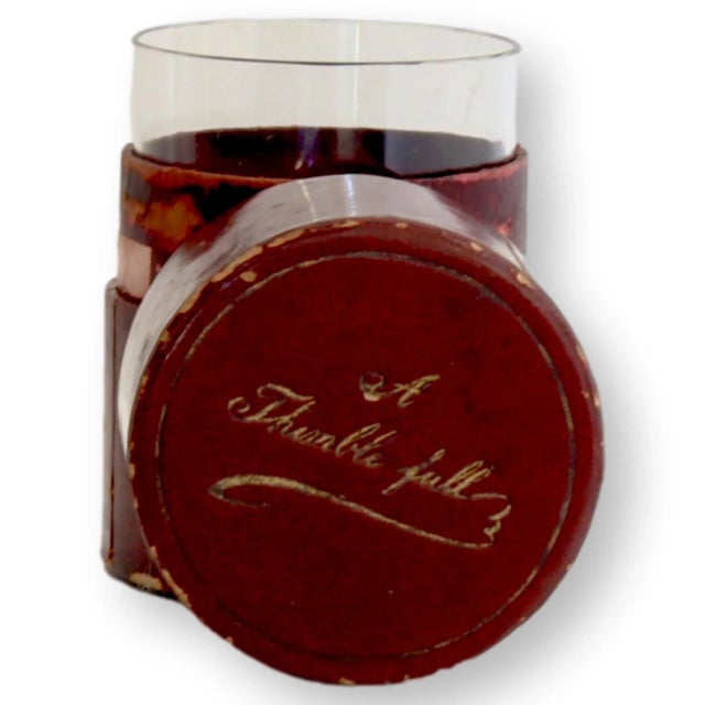 A thimble full, indeed. This 1920s English travel shot glass comes housed in its original oxblood red leather case, hand-...