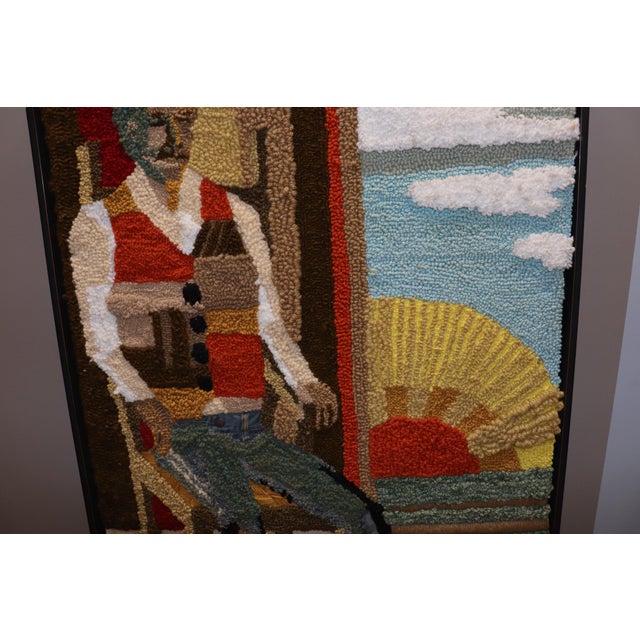 An American hooked rug mounted on a large frame with a man sitting on a chair. the material used on his pants are from raw...