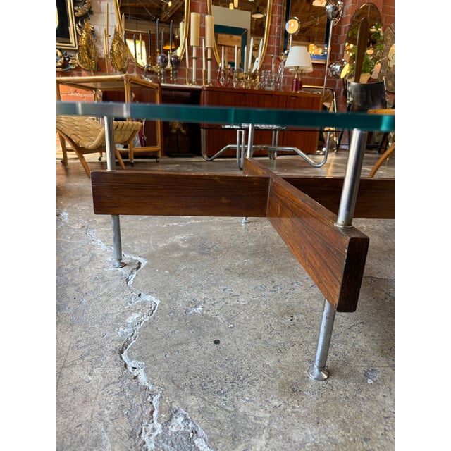 Sophisticated mid-century modern coffee table featuring a thick circular glass top resting on a sculptural rosewood X-form...