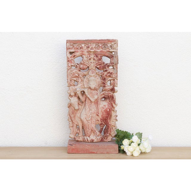 This vintage cast stone panel depicts the divine Krishna in a serene, leafy landscape, enchanting listeners with his flute...